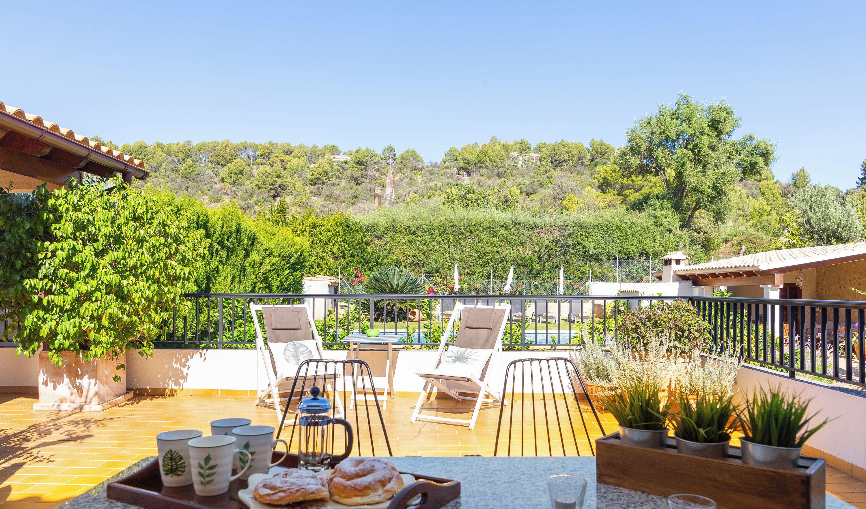 A terrace with outdoor seating, a table with pastries, and a view of a hillside.