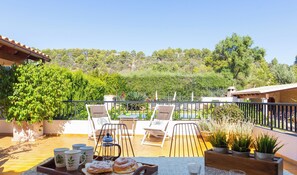 Une terrasse avec des sièges extérieurs, une table garnie de pâtisseries et une vue sur une colline.