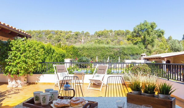 Une terrasse avec des sièges extérieurs, une table garnie de pâtisseries et une vue sur une colline.