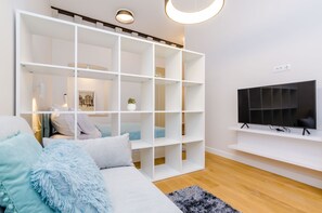 Un salon moderne avec un canapé, une étagère blanche, un téléviseur à écran plat et un plancher en bois.
