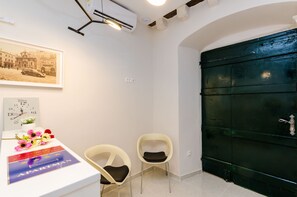 Une pièce avec une porte verte, des murs blancs et un tableau encadré accroché au mur. On y trouve deux chaises et une table sur laquelle est posée une affiche.