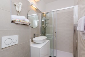 Une salle de bain moderne avec une douche à parois de verre, un lavabo blanc et un porte-serviettes orné de serviettes colorées.