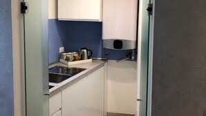 Una cocina estrecha con armarios blancos, horno empotrado y cafetera sobre la encimera.