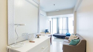 Une chambre d’hôtel moderne avec une coiffeuse blanche, un canapé et une grande fenêtre avec des rideaux.