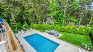 A swimming pool with a wooden deck, white lounge chairs, and a grassy lawn.
