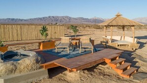 Een terras met houten meubels, een tafeltje en een prieeltje.