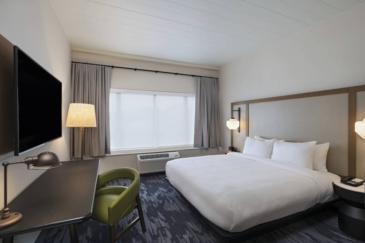 A hotel room with a bed, a desk, a chair, a television, and a window with curtains.