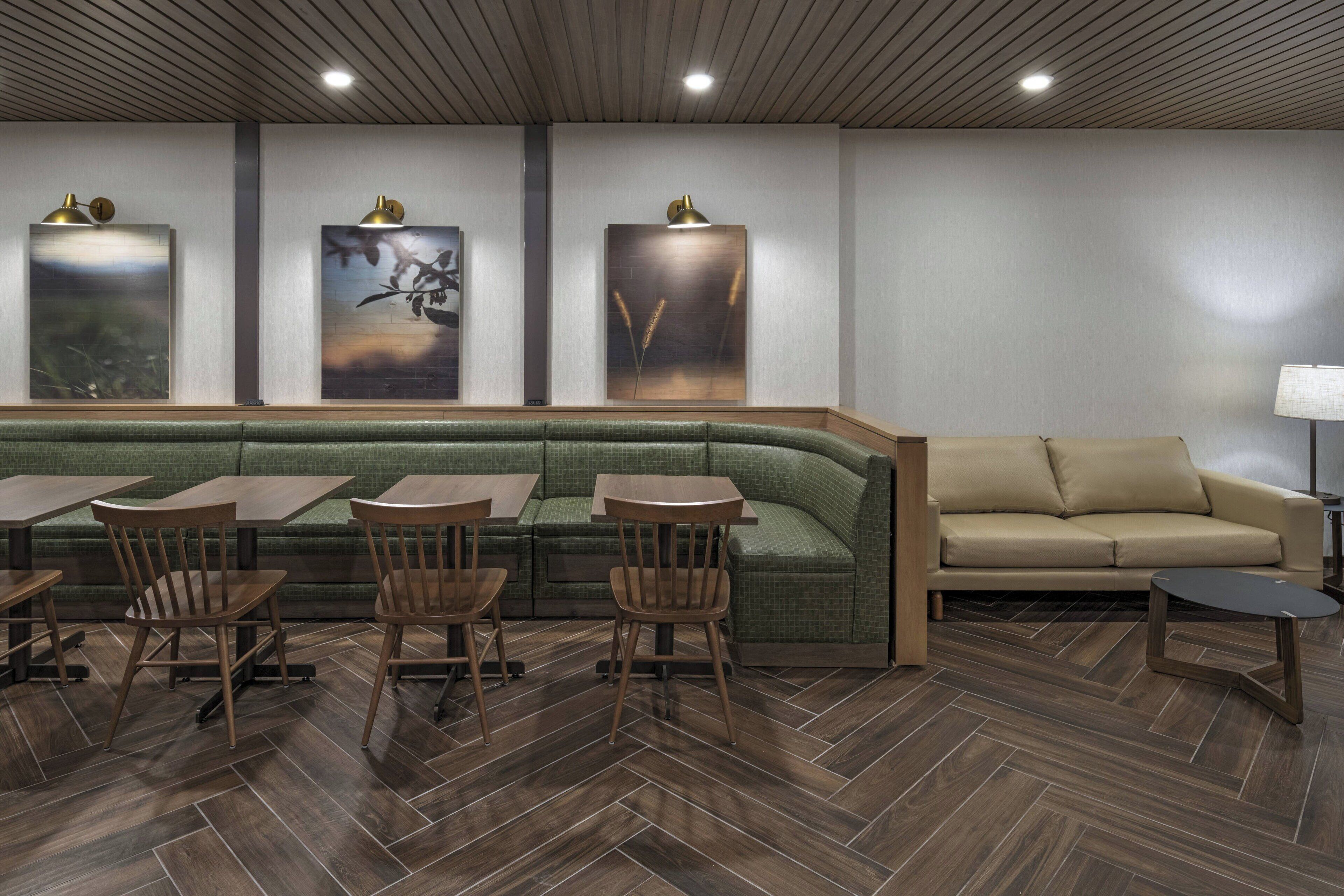 A modern restaurant with a green cushioned bench, wooden tables, and chairs.