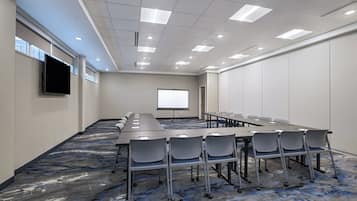 A conference room with a long table, chairs, a projector screen, and a television.