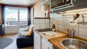 A compact kitchen with a microwave, sink, and a small appliance. There's a bottle of champagne and glasses on the counter, and a wooden bench in the living area. - Le Curling A (Val Claret) by Interhome (Tignes)