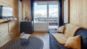 A cozy room with wooden walls, a sofa, a TV, and a view of snow-capped mountains. - Le Curling A (Val Claret) by Interhome (Tignes)