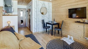 A cozy room with a wooden ceiling, a sofa, a dining table with chairs, and a TV mounted on the wall. - Le Curling A (Val Claret) by Interhome (Tignes)