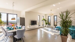 A spacious living area with a dining table, chairs, a flat-screen TV, and large windows offering a view of the outdoors. - Luxurious home in Glavina Donja (Glavina Donja)