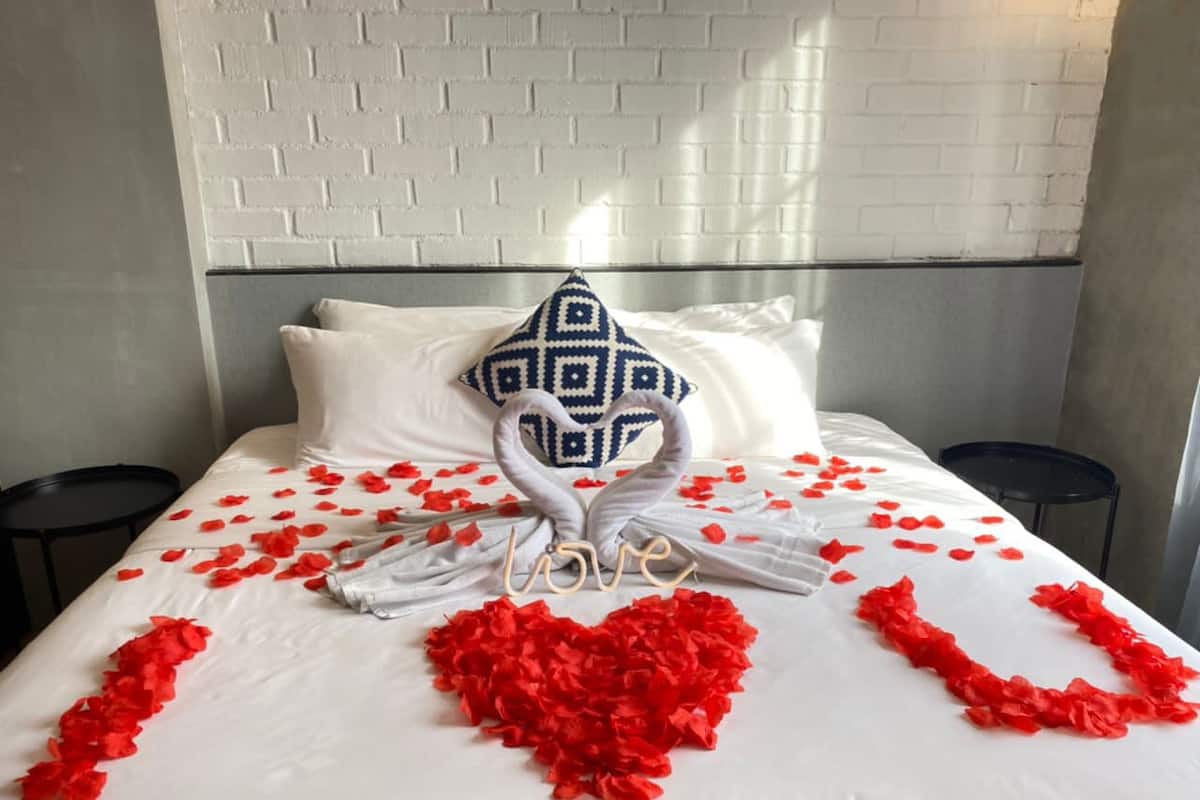 A bed with white linens, a heart-shaped arrangement of red rose petals, and a towel sculpture spelling "love" in the center.
