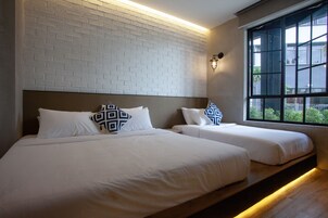 A hotel room with two beds, white bedding, a brick wall, and a window with a view.