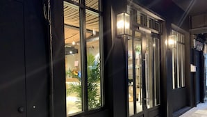 En bygnings sorte facade med store vinduer og en dør, der præsenterer et moderne design med synlige konstruktionselementer og indvendig belysning.