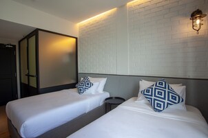 A hotel room with two single beds, a small round table, and a white brick-patterned wall.