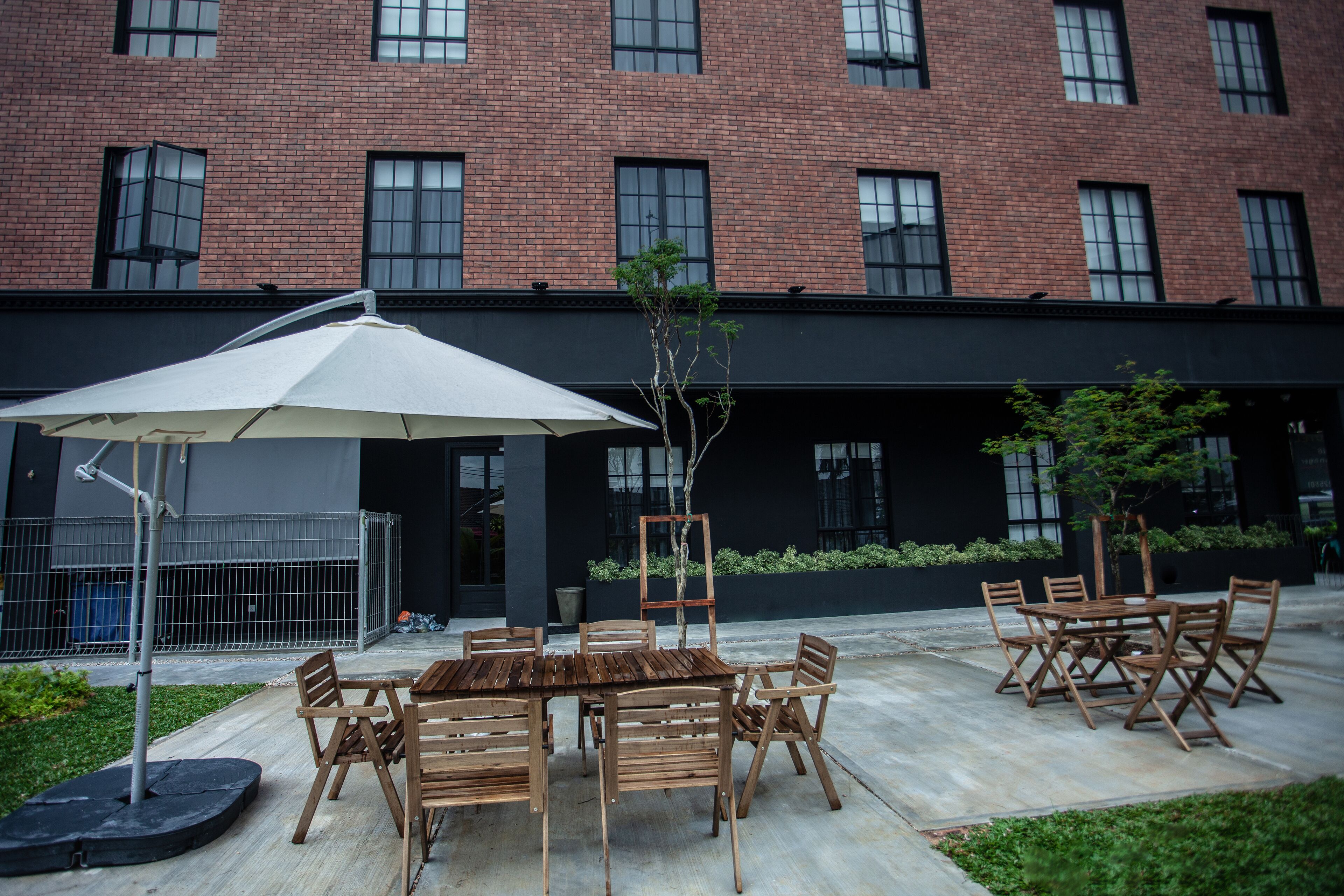 An outdoor seating area with a table and chairs, a white umbrella, and a brick building in the background.