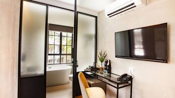 A modern bathroom with a bathtub, toilet, and a desk with a chair and a phone.