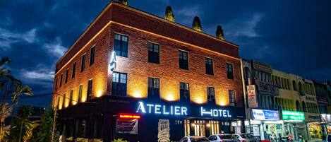 Un hotel con fachada de ladrillo, señalización iluminada y coches aparcados delante.