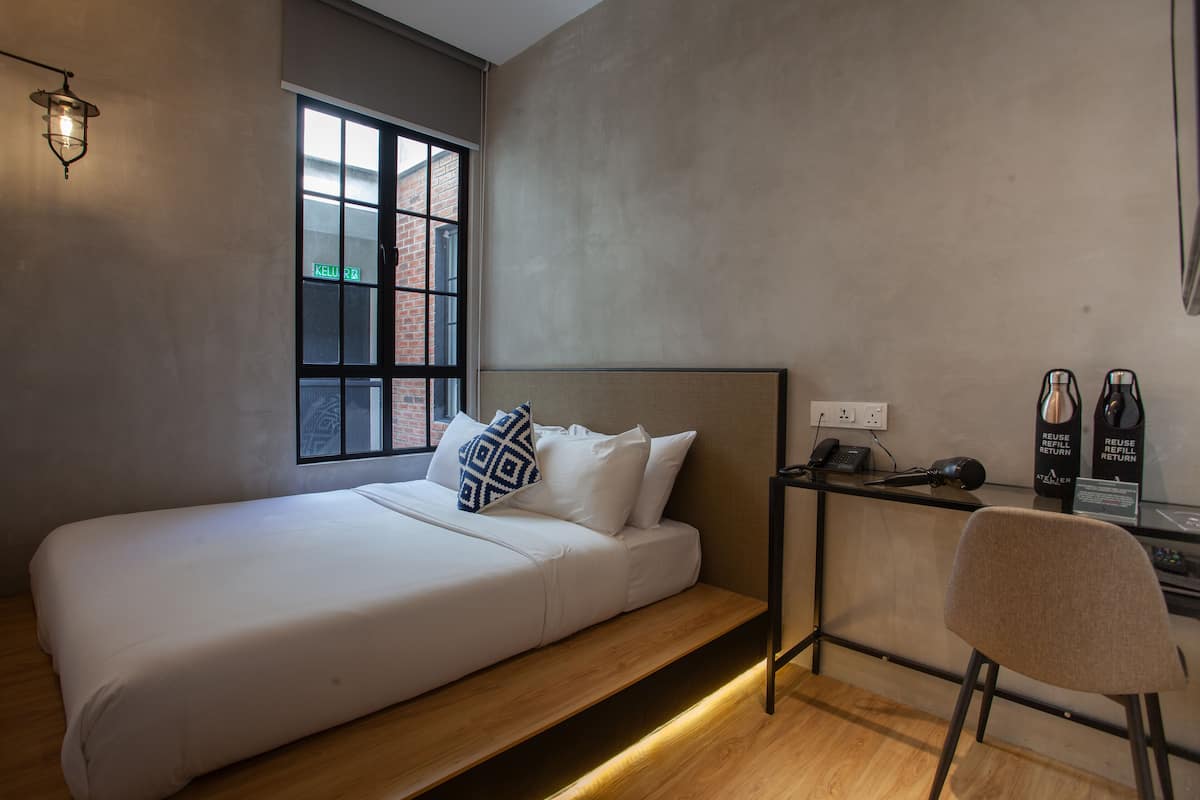 A minimalist bedroom with a single bed, a desk with a chair, and a window with a view of a brick building.