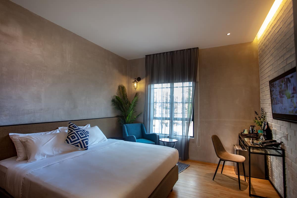 A modern hotel room with a large bed, a desk with a chair, a small table, and a large window with curtains.