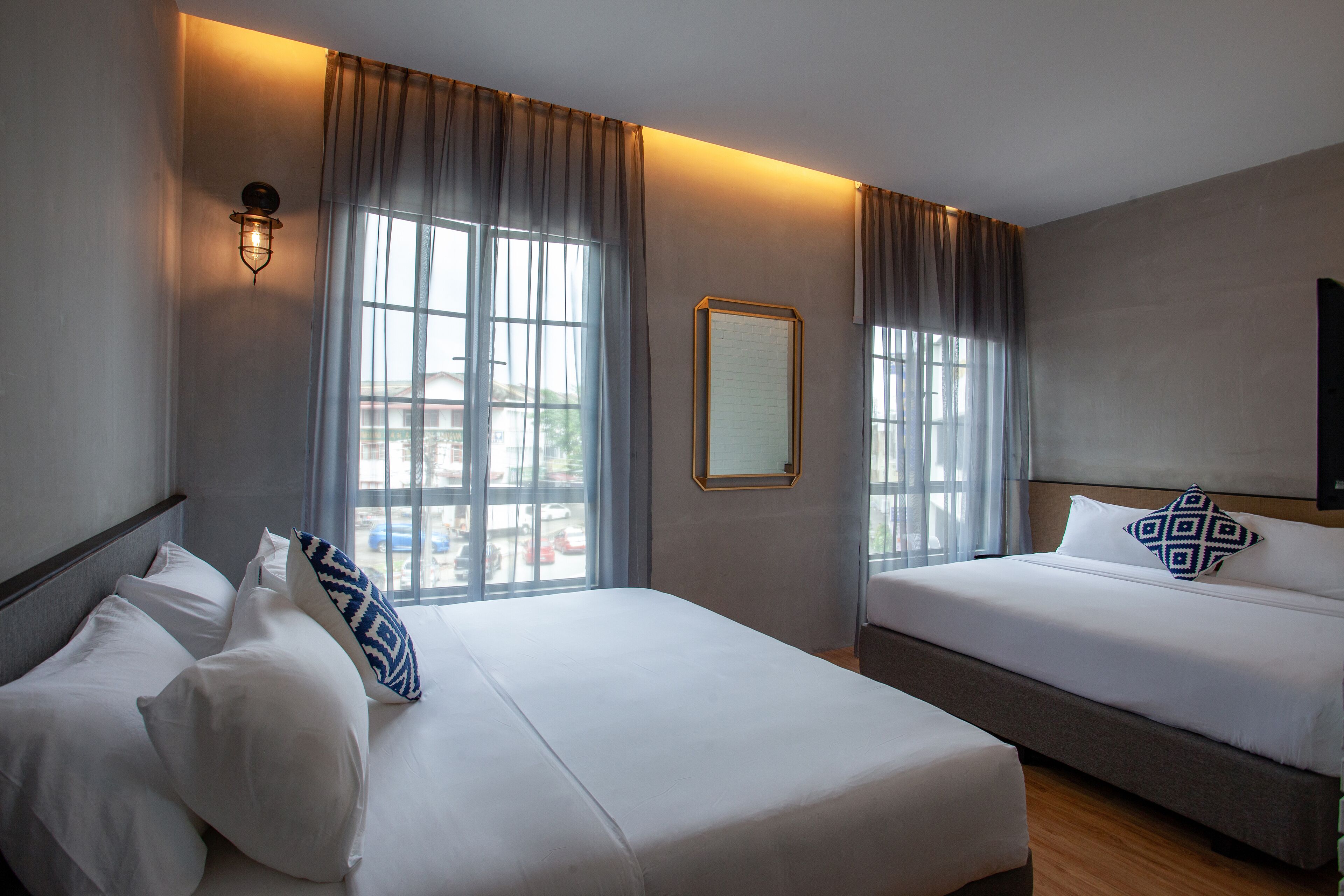 Una habitación de hotel con dos camas, un ventanal con cortinas, una lámpara de pared y un cuadro enmarcado.