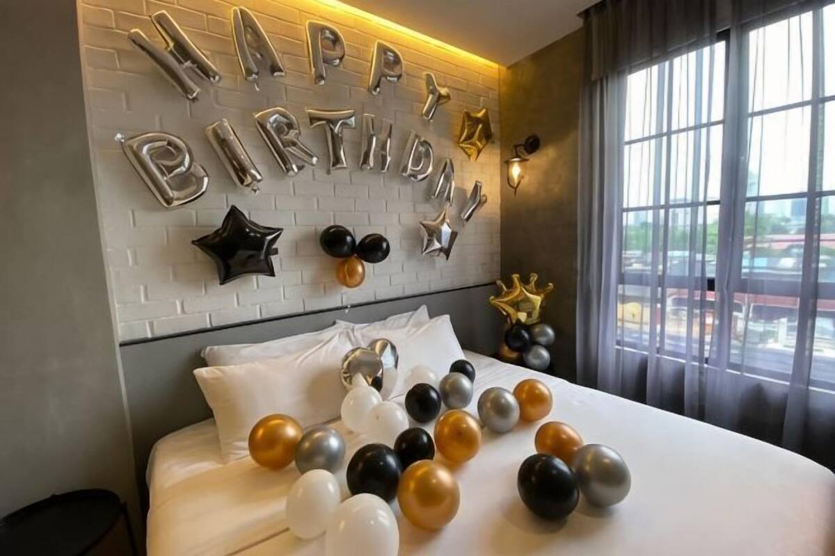 A bedroom with a bed, balloons, and a wall decoration saying 'HAPPY BIRTHDAY'.