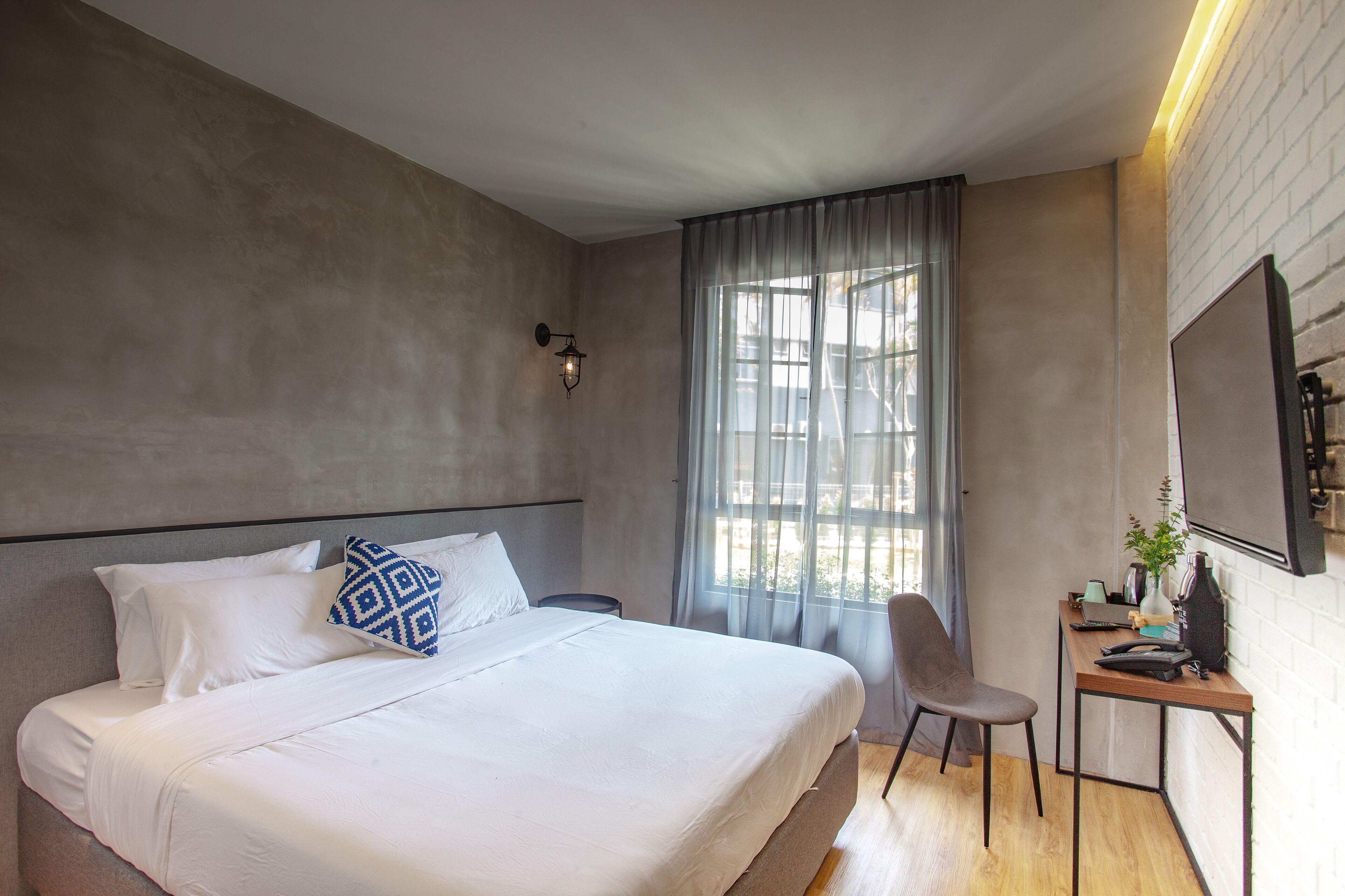 Une chambre d’hôtel moderne dotée d’un grand lit, d’un bureau avec une chaise, d’une fenêtre avec des rideaux et d’un téléviseur fixé au mur.