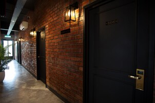 A hallway with a brick wall, a black door with a gold handle, and a sign above the door.