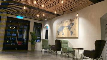 Eine Lobby mit einer Wandmalerei einer Weltkarte, modernen Sesseln und einer Decke mit hängenden Leuchten.