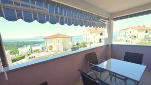 A balcony with a table and chairs, overlooking a coastal town with buildings and a view of the sea. - Apartment Marjolovic 1 (Njivice)