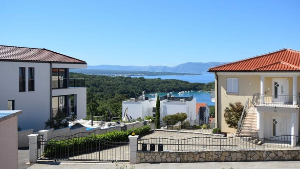 A coastal residential area with modern houses, a clear view of the sea, and a mountainous backdrop. - Apartment Marjolovic 1 (Njivice)