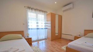 A hotel room with two beds, a wardrobe, an air conditioning unit, and a window with curtains. - Apartment Marjolovic 1 (Njivice)