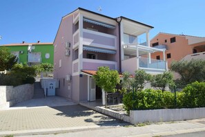 En flervåningsbostadsbyggnad med balkonger, en stenlagd entré och omgivande grönska.