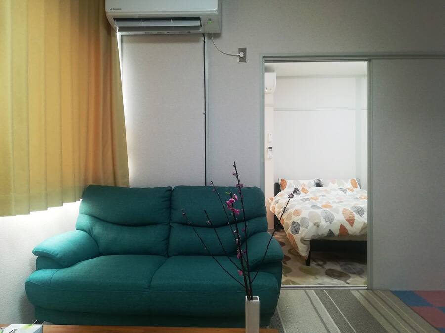 Un divano color acquamarina, un vaso con rami e un letto con biancheria decorata.