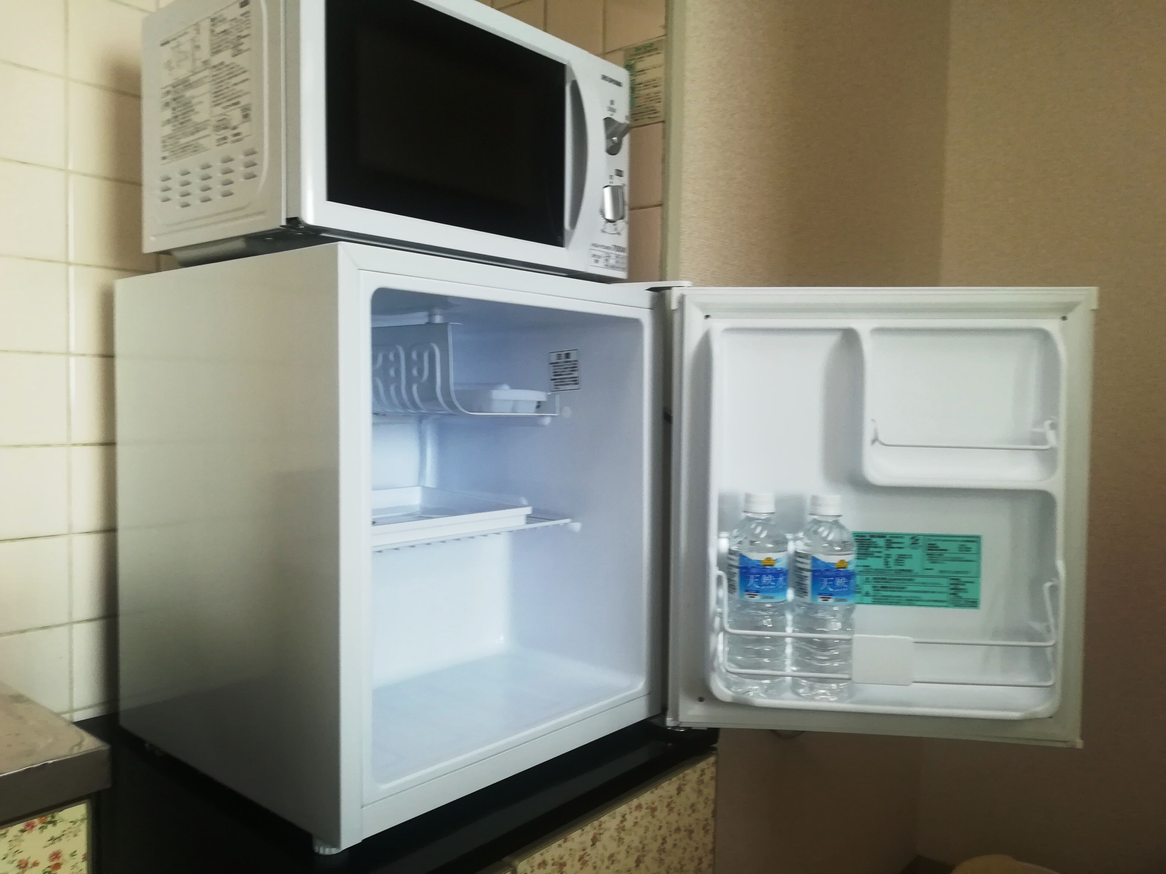 A compact refrigerator with a microwave on top, containing two water bottles and a green label.