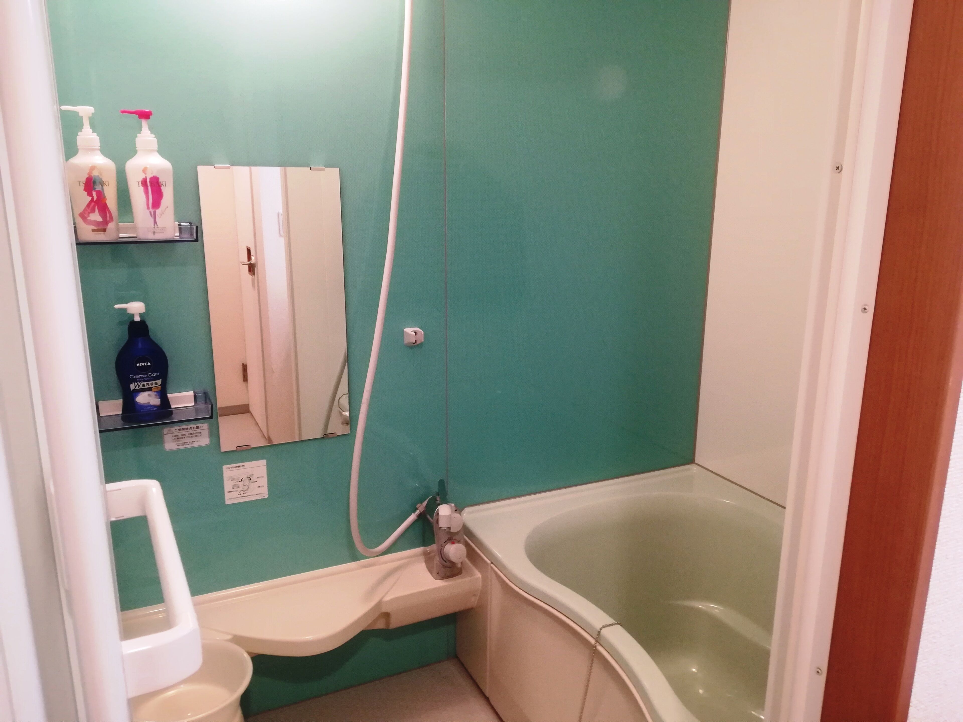 A bathroom with a green wall, a white sink, a white toilet, a white bathtub, and two bottles of shampoo on a shelf.