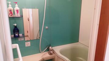 A bathroom with a green wall, a white sink, a white toilet, a white bathtub, and two bottles of shampoo on a shelf.