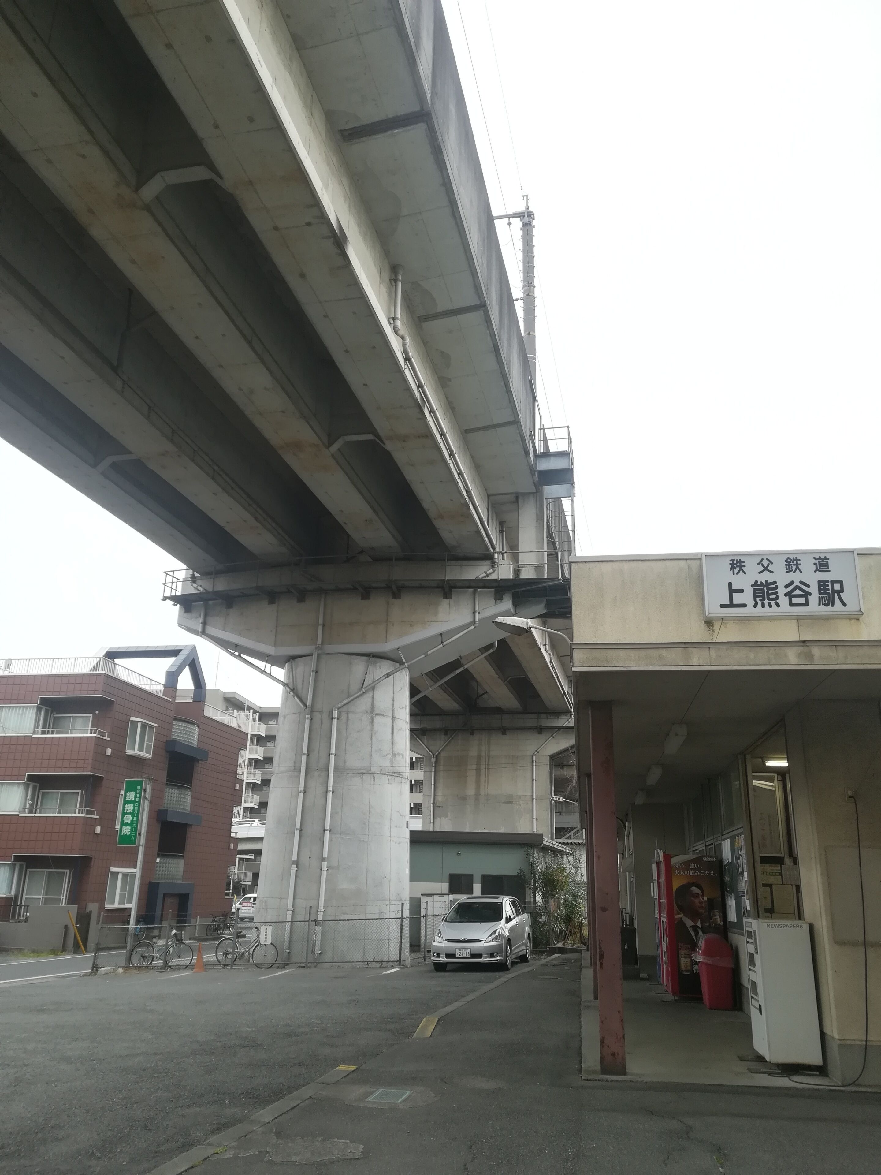 Un espace de stationnement situé sous un pont, avec une voiture, un bâtiment portant une enseigne et un kiosque à journaux.
