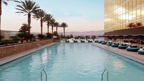 A swimming pool with lounge chairs and umbrellas, surrounded by palm trees and a modern building. - 2. 2 miles to convention center (Las Vegas)