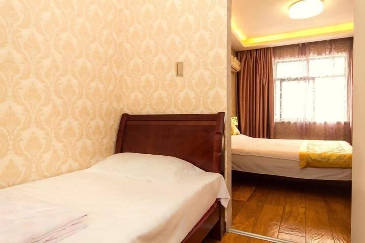 A hotel room with two beds, patterned wallpaper, a wooden floor, and a window with curtains.