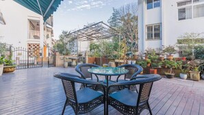 An outdoor patio with a glass table and wicker chairs, surrounded by potted plants and a metal pergola structure. - Tea farmer Inn in West Lake Hangzhou (Hangzhou)