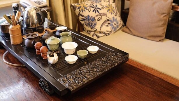 A traditional tea set on a tray with various tea utensils and cups, placed on a wooden table in a room with a sofa and a patterned pillow. - Tea farmer Inn in West Lake Hangzhou (Hangzhou)