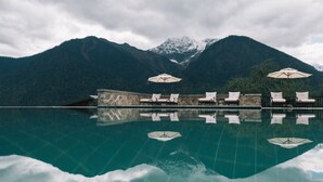 A pool with clear water reflecting the surrounding mountains and sky. There are lounge chairs and umbrellas along the poolside. - Songtsam Linka Bomi (Nyingtri)