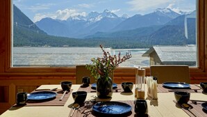 A dining table set with blue plates, bowls, and chopsticks, with a vase of flowers in the center. A window offers a view of a lake and mountains. - Songtsam Linka Bomi (Nyingtri)