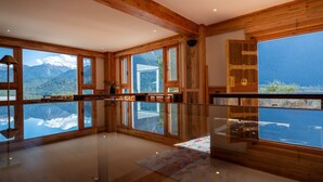 A spacious room with large windows offering mountain views, wooden beams on the ceiling, and a glass floor. - Songtsam Linka Bomi (Nyingtri)