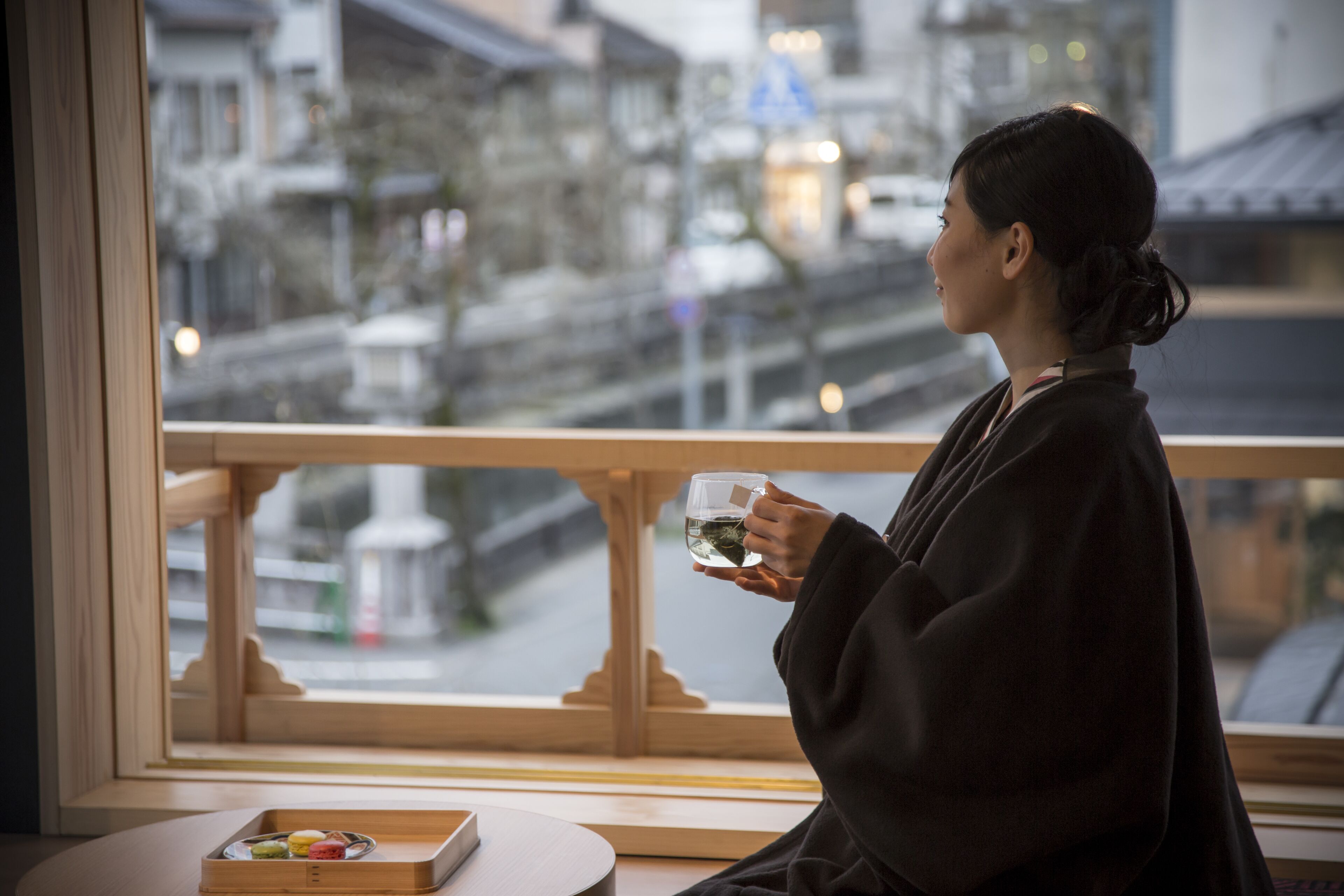 A person sitting by a window with a view of a cityscape, holding a cup.