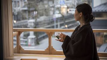 A person sitting by a window with a view of a cityscape, holding a cup.