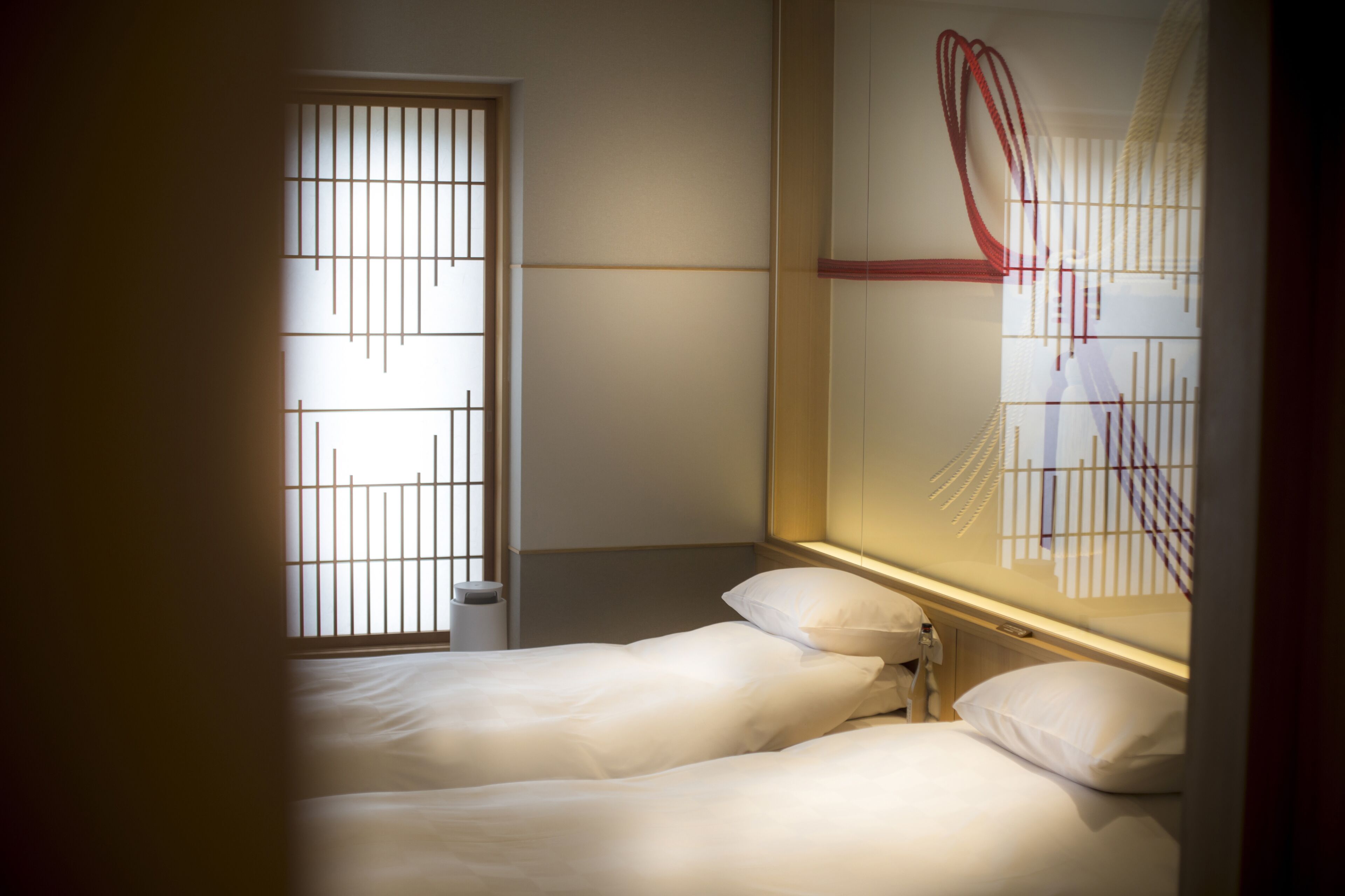 Habitación de hotel con dos camas, una ventana con rejas y una obra de arte colgada en la pared.